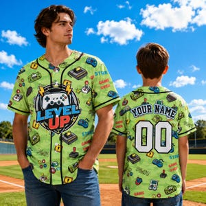 May include: A light green baseball jersey featuring an all-over print of video game controllers and consoles. The front displays a graphic with a game controller and the text LEVEL UP. The back features the text YOUR NAME and the number 00.