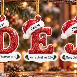 May include: Three hanging Christmas ornaments shaped as the letters D, E, and J. Each letter is red with a glittery finish, topped with a white-trimmed red Santa hat featuring the names Daniel, Emma, and Jayce. Each base says Merry Christmas 2026.