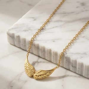 May include: A gold-toned necklace featuring a pendant shaped like a pair of symmetrical angel wings. The pendant is attached to a delicate cable chain, with the wings meeting in the center to form a curved, wing-like silhouette with detailed feather textures.