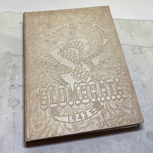 May include: Tan-colored yearbook titled "Glomerata 1943" from The Alabama Polytechnic Institute. The cover features an embossed eagle design and text. The book is slightly angled, showing its textured surface.