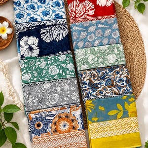 May include: A collection of ten folded rectangular cotton fabrics featuring diverse patterns including floral, seashell, and geometric motifs in vibrant colours such as red, blue, green, yellow, orange, and grey, arranged in two vertical stacks.