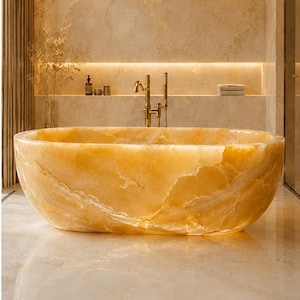 May include: A freestanding oval bathtub crafted from translucent golden-yellow onyx stone with natural white veining. The tub features a smooth, polished surface and is positioned in front of a matching marble wall with a gold-toned faucet fixture.