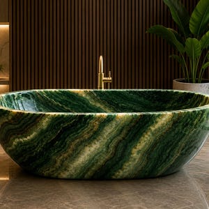 Puede incluir: Una bañera ovalada independiente fabricada en piedra verde pulida con vetas blancas y verde oscuro. La bañera presenta un exterior liso y redondeado, acompañada de un grifo alto y delgado de metal en tono dorado.