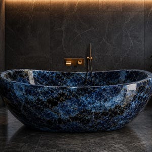 Puede incluir: Una bañera ovalada independiente con un patrón de mármol azul y negro pulido con acabado brillante. La bañera cuenta con un grifo de pared en oro cepillado y un rociador de ducha de mano a juego centrado sobre el lavabo.