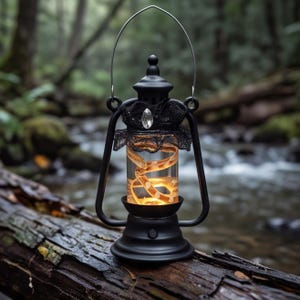 May include: A black metal lantern with a clear glass center containing a coiled, light-up snake figure. The lantern features a silver wire handle, a black lace collar around the top, and a single clear crystal accent on the front.