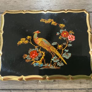 May include: A rectangular black compact mirror with a gold-toned metal frame and scalloped edges. The center features a colorful illustration of a long-tailed pheasant perched on a branch surrounded by red and pink flowers with green leaves.