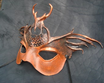 May include: A copper-colored leather masquerade mask with intricate details, including a stylized antler design and a textured pattern on the forehead.