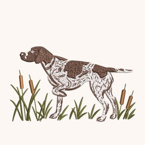 May include: An embroidered design of a brown and white German Shorthaired Pointer dog standing in a pointing stance. The dog is surrounded by green grass and brown cattails, rendered with detailed stitching on a plain light background.