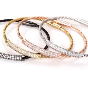 May include: Five cable bracelets with a row of clear cubic zirconia stones on the front. The bracelets are in black, gold, rose gold, and silver.