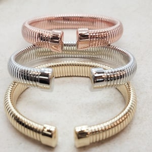 Può includere: Tre braccialetti a catena di serpente dorati, argentati e oro rosa. I braccialetti sono impilati uno sopra l'altro.