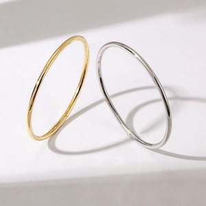 以下が含まれることがあります： 白い表面に、シンプルな薄い金属製の輪が2つ、1つは金色、もう1つは銀色で置かれています。輪はどちらも円形で、滑らかで磨かれた仕上げになっています。