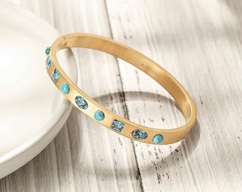 May include: A gold bangle bracelet with turquoise and blue gemstones. The bracelet is open and has a hinged clasp.