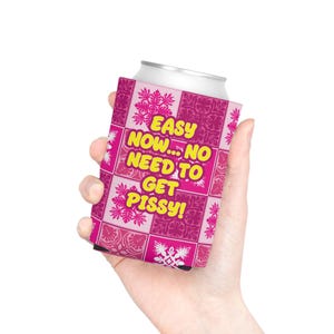 May include: A pink can cooler featuring a grid of floral patterns in varying shades of pink. The text "EASY NOW... NO NEED TO GET PISSY!" is printed in bold yellow letters across the center of the can cooler, which is wrapped around a silver can.