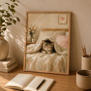 Könnte beinhalten: Ein gerahmter Kunstdruck mit einem Gemälde eines getigerten Kätzchens, das unter einer strukturierten weißen Decke auf einem Bett liegt. Die Szene zeigt eine Blumenvase, ein rosa Kissen und ein kleines Herzbild an der Wand in neutralen Farben.