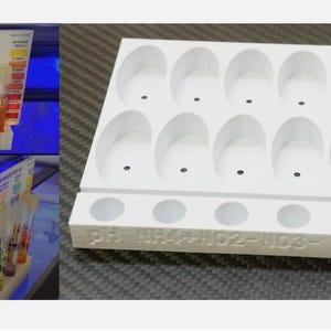 May include: A white 3D-printed organizer stand for a freshwater master test kit. The stand features ten oval-shaped slots for test tubes and six circular holes for reagent bottles, with labels pH, NH4, NO2, NO3, GH, and KH embossed on the front edge.