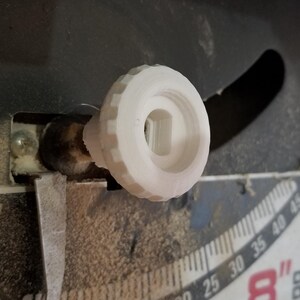 May include: A white, circular, 3D-printed adjustment knob with a textured, ridged outer edge and a central square-shaped opening, attached to a metal shaft on a piece of machinery featuring a scale with the number 8 visible in red.