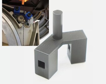 Può includere: Un blocco guida in plastica grigio scuro stampato in 3D, dotato di un montante cilindrico verticale e di una base a forma di U con due ritagli quadrati. Il componente è mostrato accanto a una vista ravvicinata di una guida per sega a nastro.