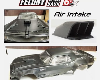 Może przedstawiać: Matowa czarna karoseria do zdalnie sterowanego samochodu Felony Street Bash 6S BLX. Zestaw zawiera oddzielny czarny wlot powietrza z trzema wewnętrznymi przegrodami. Karoseria posiada wlot na masce, przednią szybę oraz boczne otwory wentylacyjne.