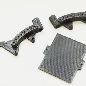 May include: Three black 3D printed components consisting of two identical curved brackets with multiple circular holes and one rectangular plate featuring a diagonal textured surface pattern, all displaying visible layer lines from the printing process.