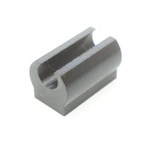 May include: A dark gray, rectangular plastic component featuring a cylindrical channel running along its top surface. The object has a flat base and a textured finish, with visible horizontal layer lines indicating a 3D printed construction.