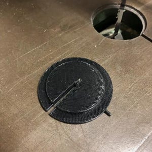 May include: A black, circular, 3D-printed insert for a bandsaw table. The disc features a textured surface, a central slot, and a small protruding tab on the outer edge, designed to fit into the circular throat plate opening of a bandsaw.