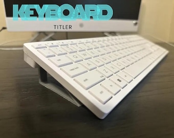 Może przedstawiać: Biała klawiatura komputerowa spoczywająca na szarej, nachylonej podstawce. Klawiatura posiada standardowy układ QWERTY z białymi klawiszami i czarnymi literami. Tekst KEYBOARD TITLER jest wyświetlany niebieską czcionką w stylu retro powyżej.