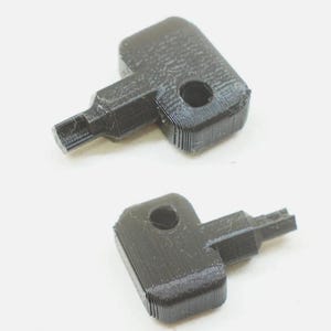 May include: Two black, 3D-printed plastic keys with a rectangular head featuring a circular hole and a stepped, narrow shaft. The surface of the keys shows visible horizontal layer lines from the manufacturing process, creating a textured finish.