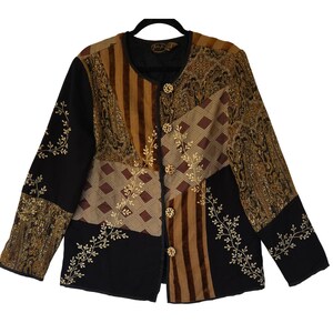 May include: A long-sleeved jacket featuring a patchwork design of black, brown, and tan panels. The garment includes sections with striped, diamond, and paisley patterns, accented by gold-colored floral embroidery and five round, light-colored buttons.