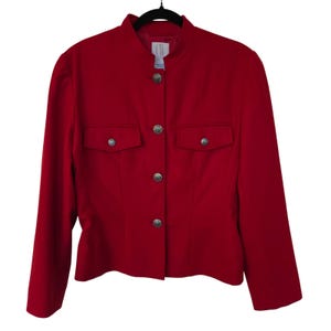 May include: A vibrant red jacket featuring a mandarin collar, long sleeves, and a front button closure. The garment includes two chest pockets with flaps, each secured with a silver-toned metal button matching the front closure buttons.