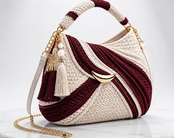 May include: A crochet handbag featuring a cream and deep burgundy color scheme with a crescent-shaped gold metal accent. The bag includes a matching crochet handle, a gold chain shoulder strap, and decorative tassels with white pearl beads.
