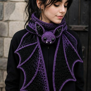 May include: A crochet scarf featuring a central purple bat head with large black eyes and white fangs. The scarf body is made of black yarn with purple trim, designed to resemble bat wings that drape down from the neck in a layered pattern.