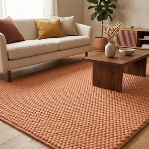 May include: A rectangular area rug featuring a textured, raised pom-pom surface in a solid terracotta orange color. The rug is constructed with a dense, repeating pattern of small, soft, rounded tufts that create a uniform, tactile appearance.