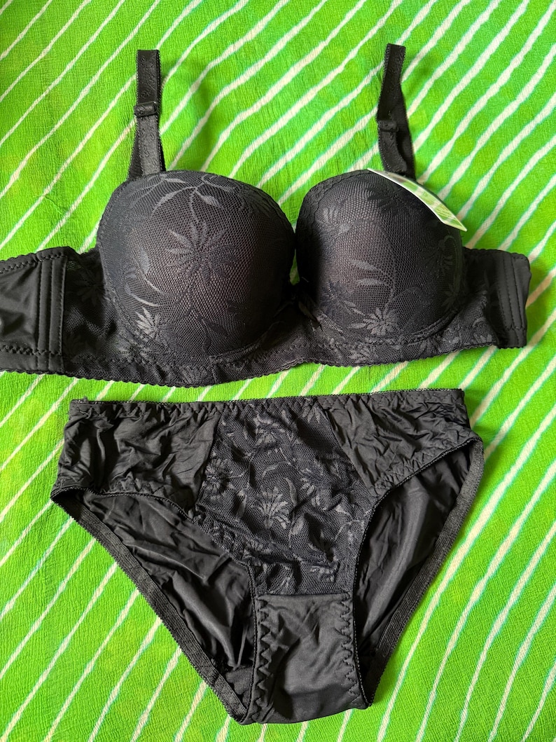 May include: A black matching lingerie set consisting of a molded cup bra with adjustable straps and a floral lace overlay, paired with coordinating high-cut briefs featuring a central floral lace panel and solid black side sections.