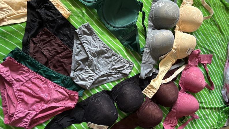 May include: A collection of assorted undergarments including several bras and panties in various colors such as black, pink, green, grey, and beige. The bras feature molded cups with a subtle floral pattern, while the panties are solid-colored.