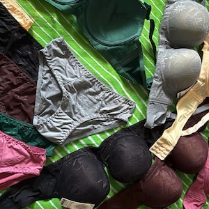 May include: A collection of assorted undergarments including several bras and panties in various colors such as black, pink, green, grey, and beige. The items feature textured floral patterns and solid fabric designs with adjustable straps and elastic waistbands.