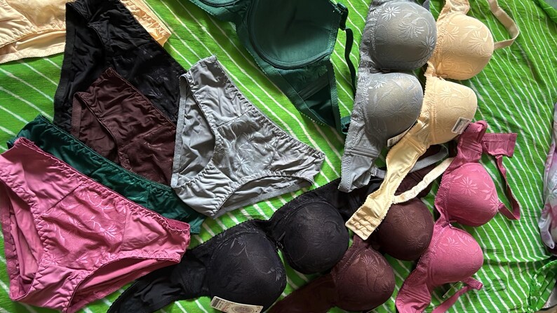 May include: A collection of assorted undergarments including several bras and panties in various colors such as black, pink, green, grey, and beige. The items feature textured floral patterns and solid fabric designs with adjustable straps and elastic waistbands.