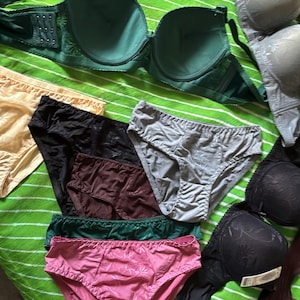 May include: A collection of assorted undergarments including several bras and panties in various colors such as green, black, gray, pink, beige, and dark brown. The items feature different textures, patterns, and styles, displayed together in a group.