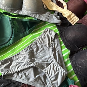 May include: A collection of undergarments including several bras and panties in various colors such as beige, gray, dark brown, green, pink, and black. The items feature textured floral patterns and are arranged together in a group.