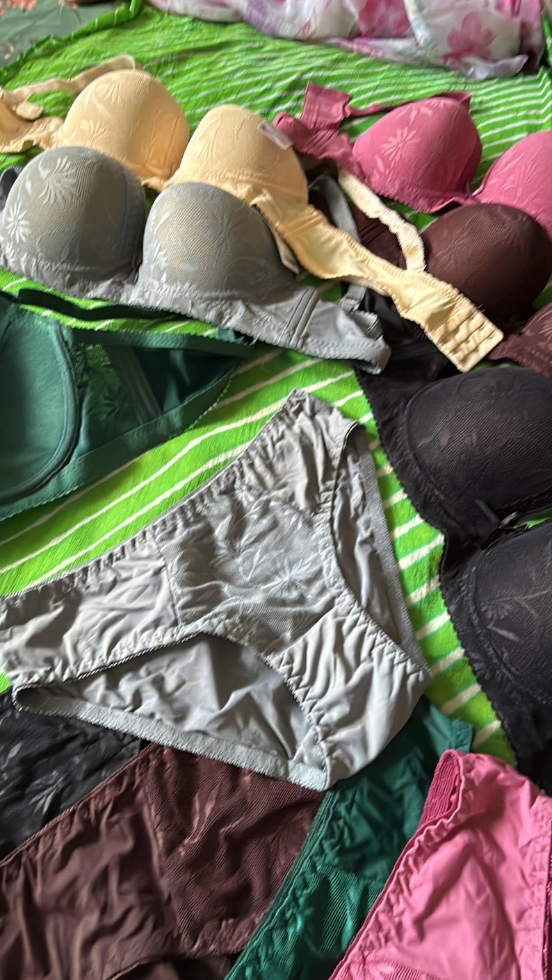 May include: A collection of undergarments including several bras and panties in various colors such as beige, gray, dark brown, green, pink, and black. The items feature textured floral patterns and are arranged together in a group.