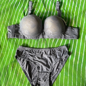 May include: A matching gray lingerie set consisting of a molded cup bra and high-cut briefs. Both pieces feature a subtle, tonal floral pattern overlaid on the fabric. The bra includes adjustable shoulder straps and a wide band, while the briefs have a smooth, solid gray back panel and a patterned front panel.