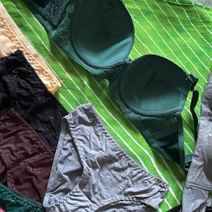 May include: A collection of undergarments including several pairs of briefs in beige, black, dark brown, grey, green, and pink, alongside multiple bras in dark green, grey with a floral pattern, and beige with a floral pattern.
