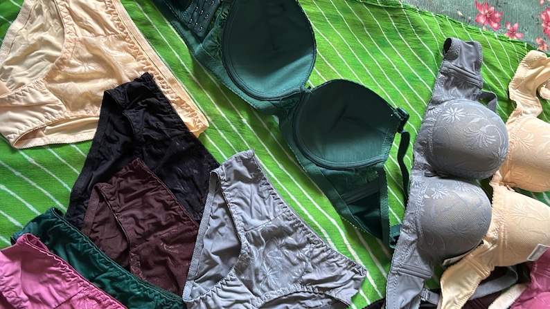 May include: A collection of undergarments including several pairs of briefs in beige, black, dark brown, grey, green, and pink, alongside multiple bras in dark green, grey with a floral pattern, and beige with a floral pattern.