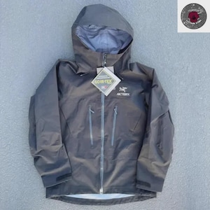 Könnte beinhalten: Eine dunkelgraue Arc'teryx Kapuzenjacke mit durchgehendem Frontreißverschluss, zwei vertikalen Brusttaschen mit Reißverschluss und verstellbaren Ärmelbündchen. Ein Gore-Tex-Etikett ist befestigt und das Logo ist auf der Brust gedruckt.