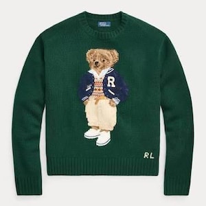Könnte beinhalten: Ein dunkelgrüner Langarmpullover mit Rundhalsausschnitt und einem Teddybären-Motiv, der eine marineblaue College-Jacke mit dem Buchstaben R, eine gemusterte Weste, eine helle Hose und weiße Schuhe trägt. Die Buchstaben RL sind unten eingestickt.