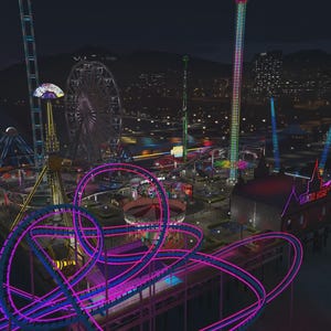 May include: An aerial night view of an amusement park on a pier featuring a bright neon pink roller coaster track in the foreground. The park includes a large Ferris wheel, tall drop towers, and a building labelled Haunted House with colourful lights.