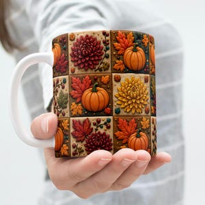 Peut inclure: Un mug en céramique blanche orné d'un motif en grille composé de carreaux carrés. Chaque carreau présente un design automnal en relief et texturé, incluant des citrouilles orange, des chrysanthèmes rouge foncé et jaune, et des feuilles d'érable.