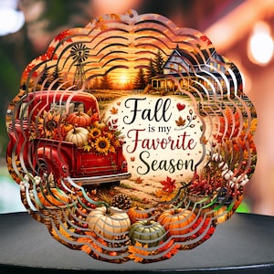 Puede incluir: Un molinillo de viento circular de metal con una ilustración otoñal de una camioneta roja llena de calabazas y girasoles, una granja y un molino. El texto "Fall is my Favorite Season" está impreso en el centro en letra oscura.