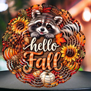 Peut inclure: Un carillon à vent circulaire en métal orné d'une illustration de raton laveur au-dessus du texte "hello Fall" en écriture blanche. Le motif comprend des citrouilles orange, des tournesols jaunes, des baies rouges, des pommes de pin et des carreaux.