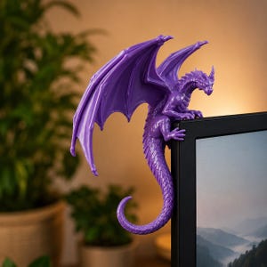 May include: A purple dragon figurine perched on the top corner of a black computer monitor. The dragon has large, spread wings, textured scales, and a long, curved tail that hangs down the side of the screen frame in a vertical position.