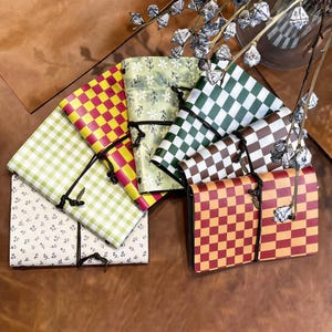 May include: A collection of six rectangular notebooks with various covers, including yellow and pink checkered, green and white floral, dark green and white checkered, brown and white checkered, red and orange checkered, and white with blue floral patterns.